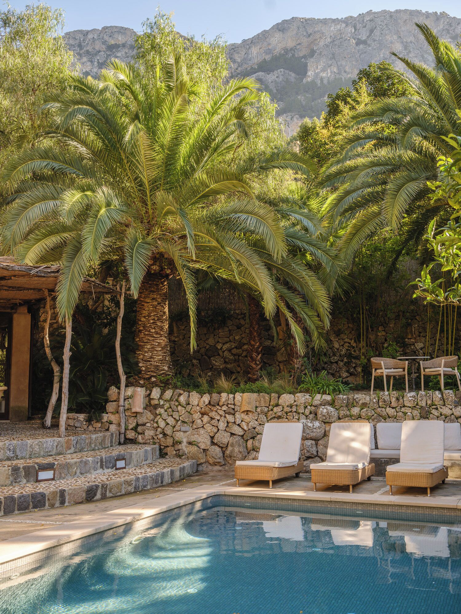 A pool area with lounge chairs, palm trees, and a stone wall.