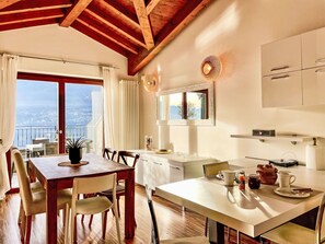 Ein Essbereich mit Holztisch und -stühlen, Meerblick durch große Fenster und eine Küche mit modernen Geräten.