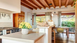 Een moderne keuken met houten balken, een centraal eiland met een bloevas, en uitzicht op groen buiten.