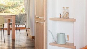 Een kamer met een houten eettafel, stoelen, een houten bank en een wandplank met planten en een gieter.