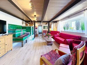 Ein gemütliches Interieur mit Holzboden, einer grünen Fliesenbank, einem roten Sofa und einem Fernseher links.