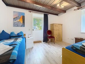 Een slaapkamer met twee bedden, een houten garderobe, een stoel en een schilderij aan de muur.