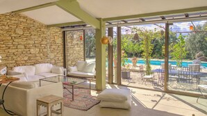 Ein geräumiger Wohnbereich mit Steinwand, weißen Möbeln und Blick auf Pool und Garten.