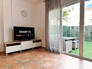 A modern living room with a flat-screen TV displaying 'SMART TV' and streaming services, a sliding glass door to a patio, and a white cabinet with drawers. - Cap Salou House: Tranquil, Shared Pool, Close to Beach (Salou)