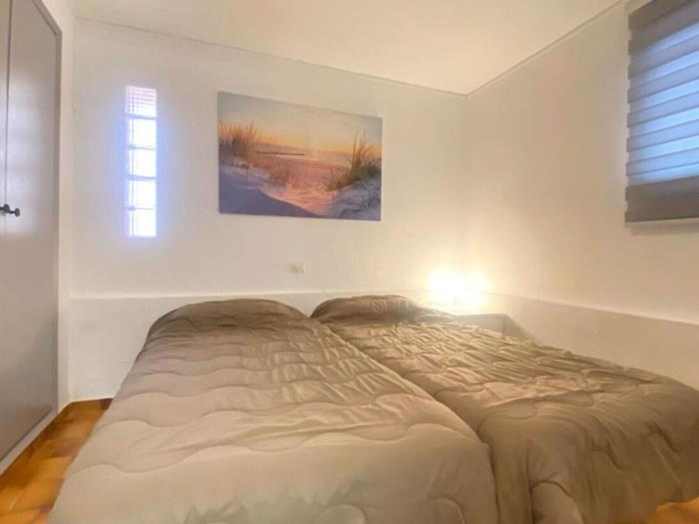 A bedroom with a bed, a window with blinds, and a painting on the wall.