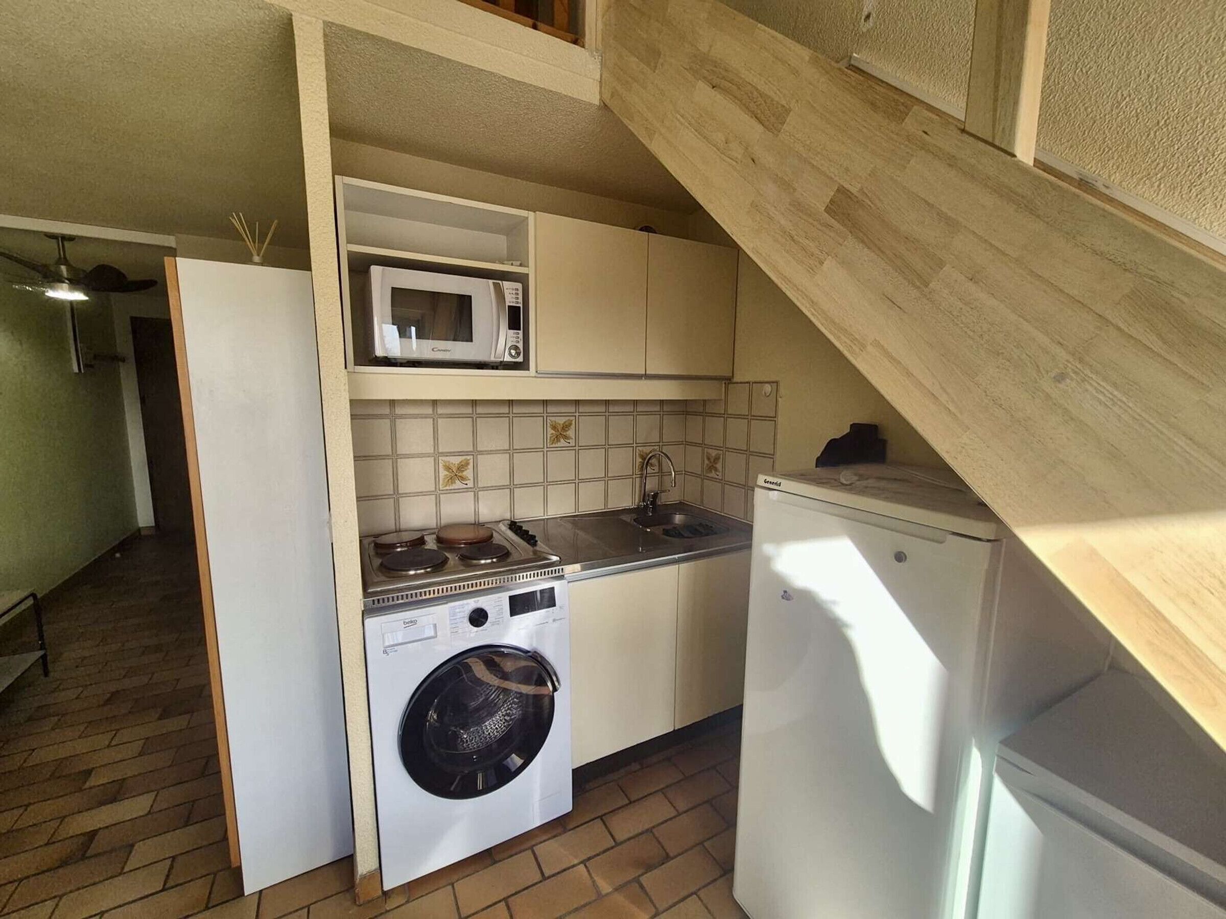 A compact kitchen with a microwave, stove, sink, and washing machine.