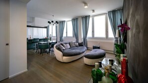 A modern living room with a curved sofa, a dining area, and a kitchen in the background. - Rosa 37 - Modern & Elegamnt 2BR Apt - Near Venice (Venezia)