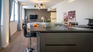 A modern kitchen with a central island, a dining area with a sofa, and a TV mounted on the wall. - Rosa 37 - Modern & Elegamnt 2BR Apt - Near Venice (Venezia)