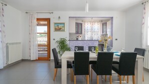 A dining area with a table set for four, chairs, a potted plant, and a view into the kitchen. - Villa Milena Vodnjan by Villas Guide (Vodnjan)