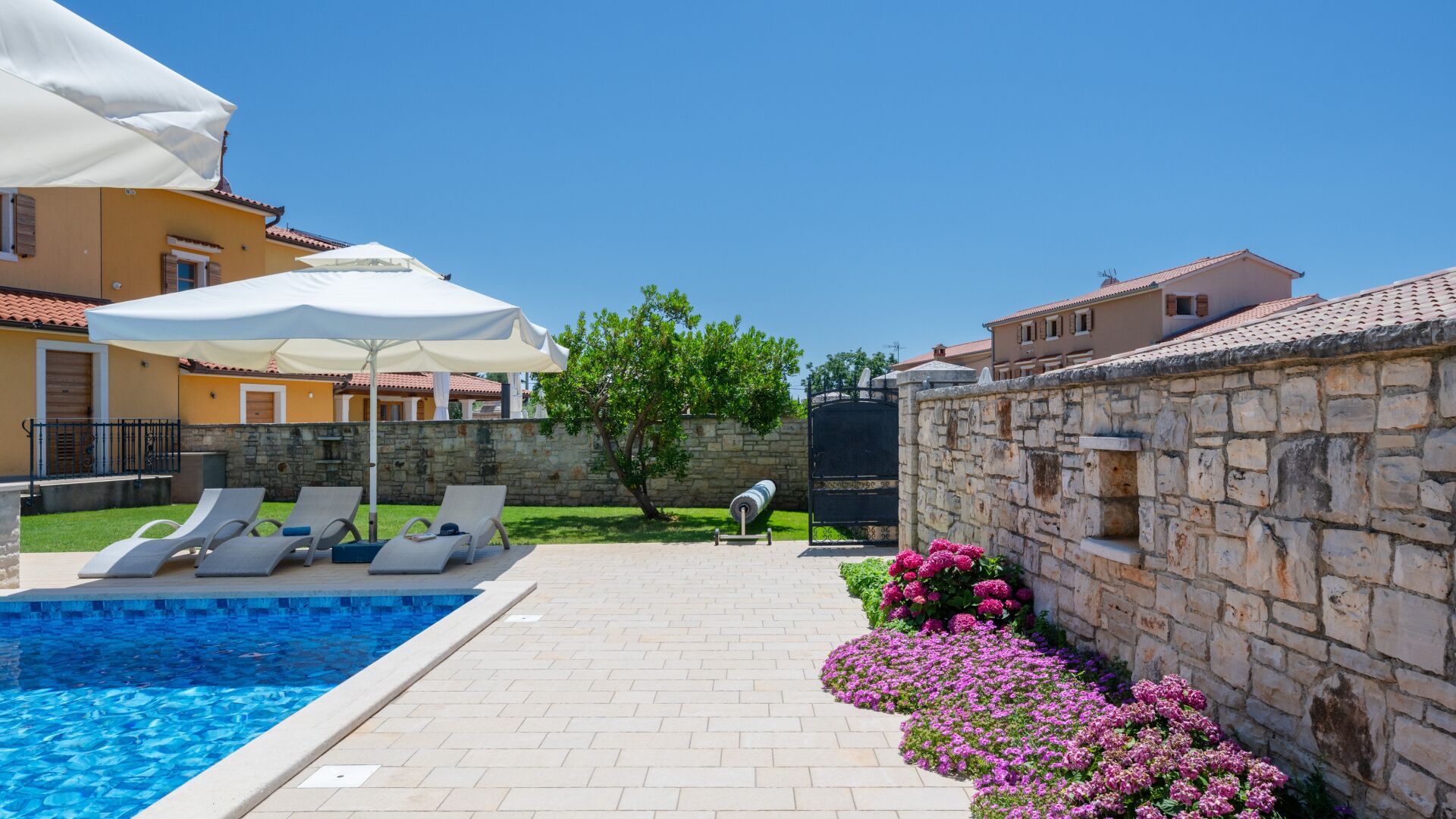 A swimming pool with lounge chairs, a stone wall, and a garden with flowers.
