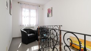 Ein Zimmer mit einem schwarzen Ledersessel, einem Metallgeländer, einem Heizkörper und einem Fenster mit durchsichtigen Vorhängen.