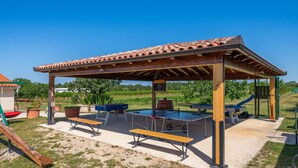 Un área recreativa al aire libre con zona de estar cubierta, mesas de billar y un tobogán.