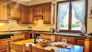 Une cuisine avec des meubles de rangement en bois, une table à manger dressée pour deux personnes et une fenêtre avec des rideaux.