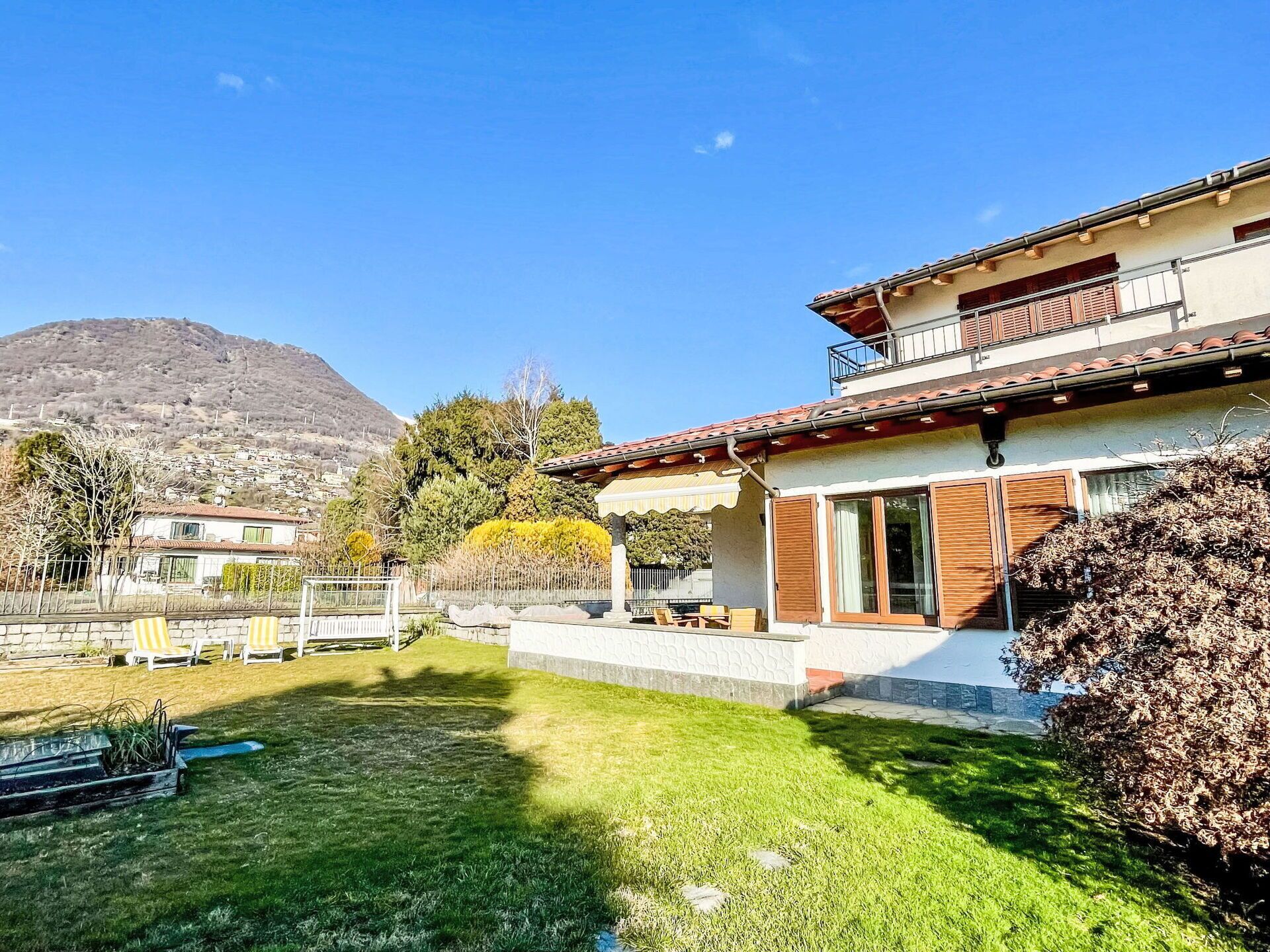 A two-story house with a balcony, a well-maintained lawn, and a mountain in the background.
