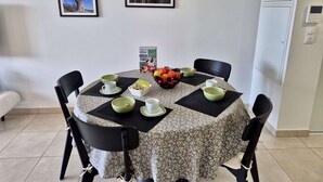 A dining area with a round table covered by a patterned tablecloth, surrounded by black chairs. There are bowls, cups, and a box of frosted flakes on the table. Two framed pictures are hung on the wall above the table. - 3-Room Apartment in Cogolin, 4 Pers with Parking Included (Cogolin)