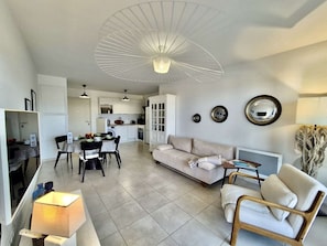 A modern living room with a sofa, chairs, a dining table, and a kitchen in the background. - 3-Room Apartment in Cogolin, 4 Pers with Parking Included (Cogolin)