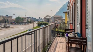 Varanda com vista para uma estrada e edifícios, uma mesa com cadeiras e um corrimão.