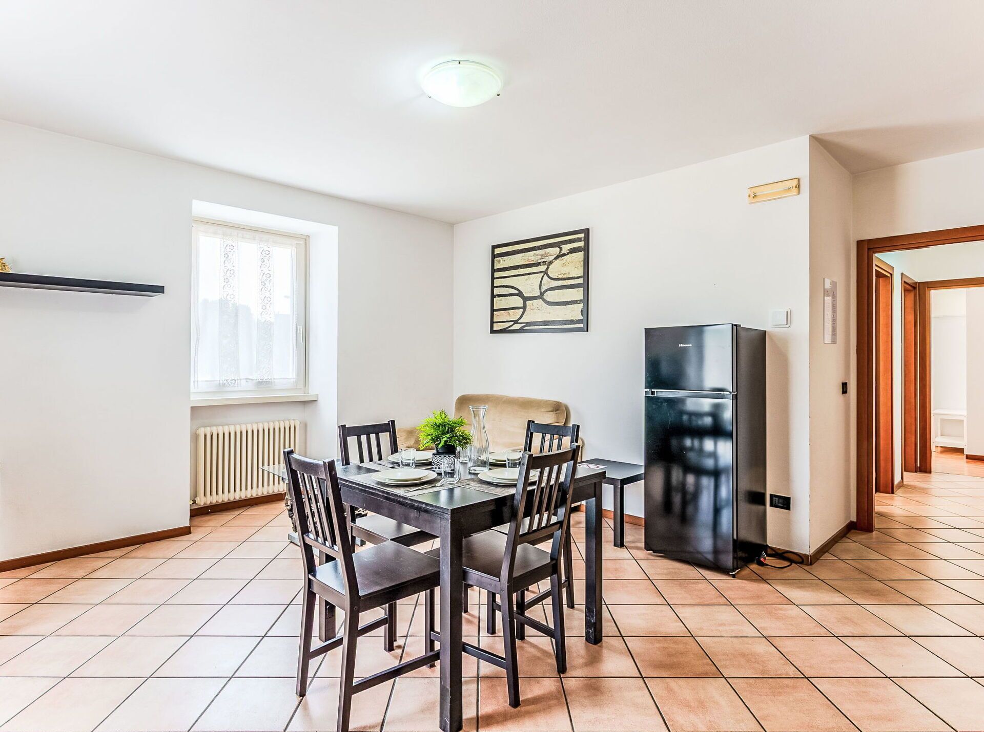 Eine moderne Küche mit Esstisch, Stühlen, einem Kühlschrank und einem Fenster mit Vorhängen.