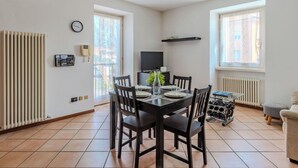 Uma sala de jantar com uma mesa posta para quatro pessoas, uma televisão na parede e um radiador.
