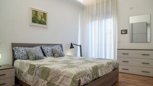 A bedroom with a bed, bedside tables, a lamp, a painting, a window with curtains, a mirror, and a wardrobe. - Cosy apartment for 4 guests with A/C, TV and balcony (Termoli)