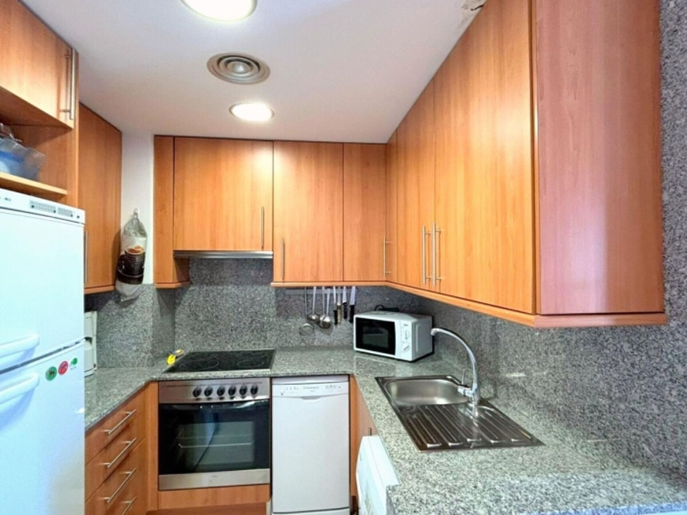 A kitchen with wooden cabinets, a built-in oven, a microwave, and a stainless steel sink.