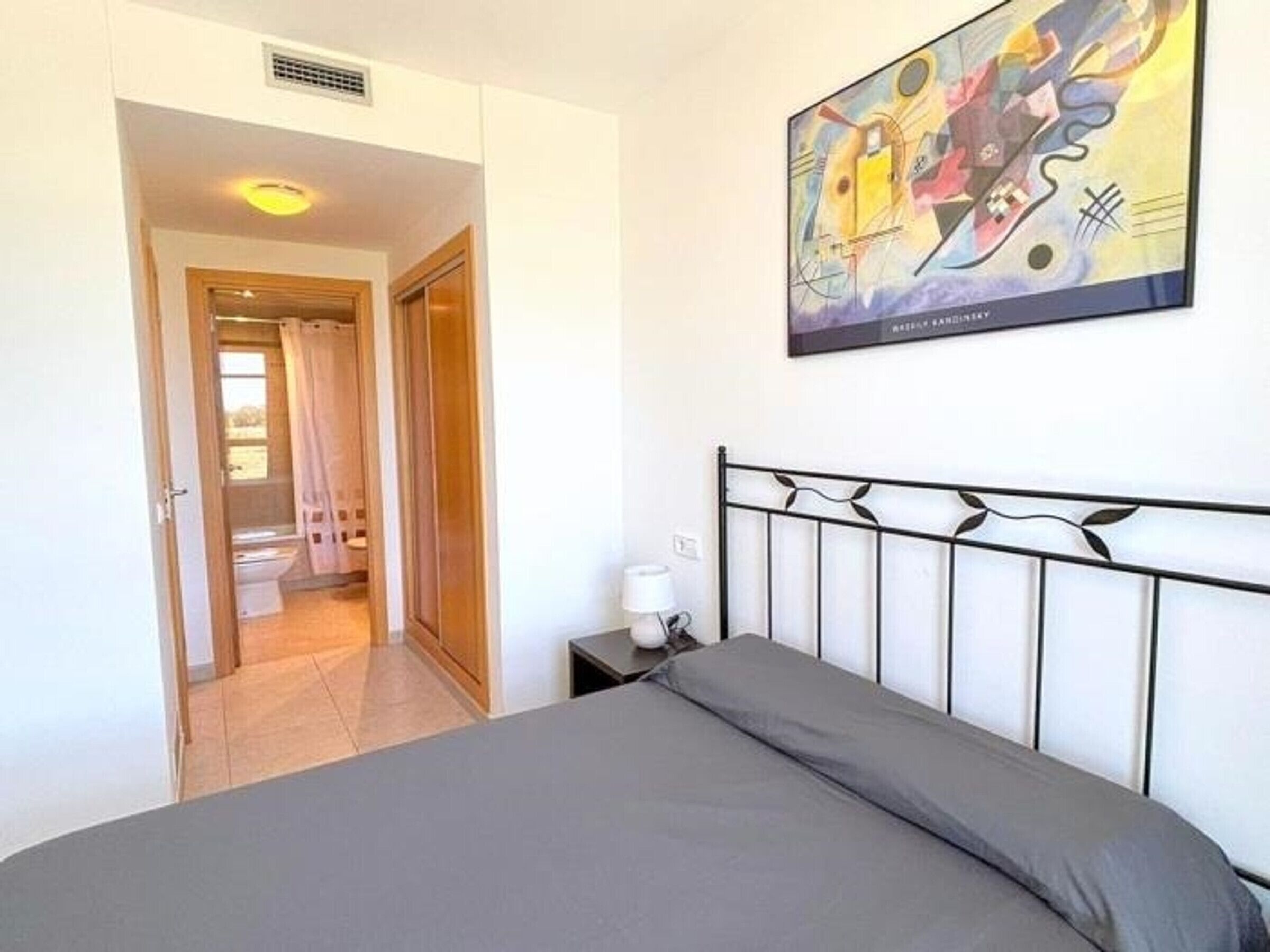 Un dormitorio con cama, mesita de noche, lámpara y un cuadro en la pared.