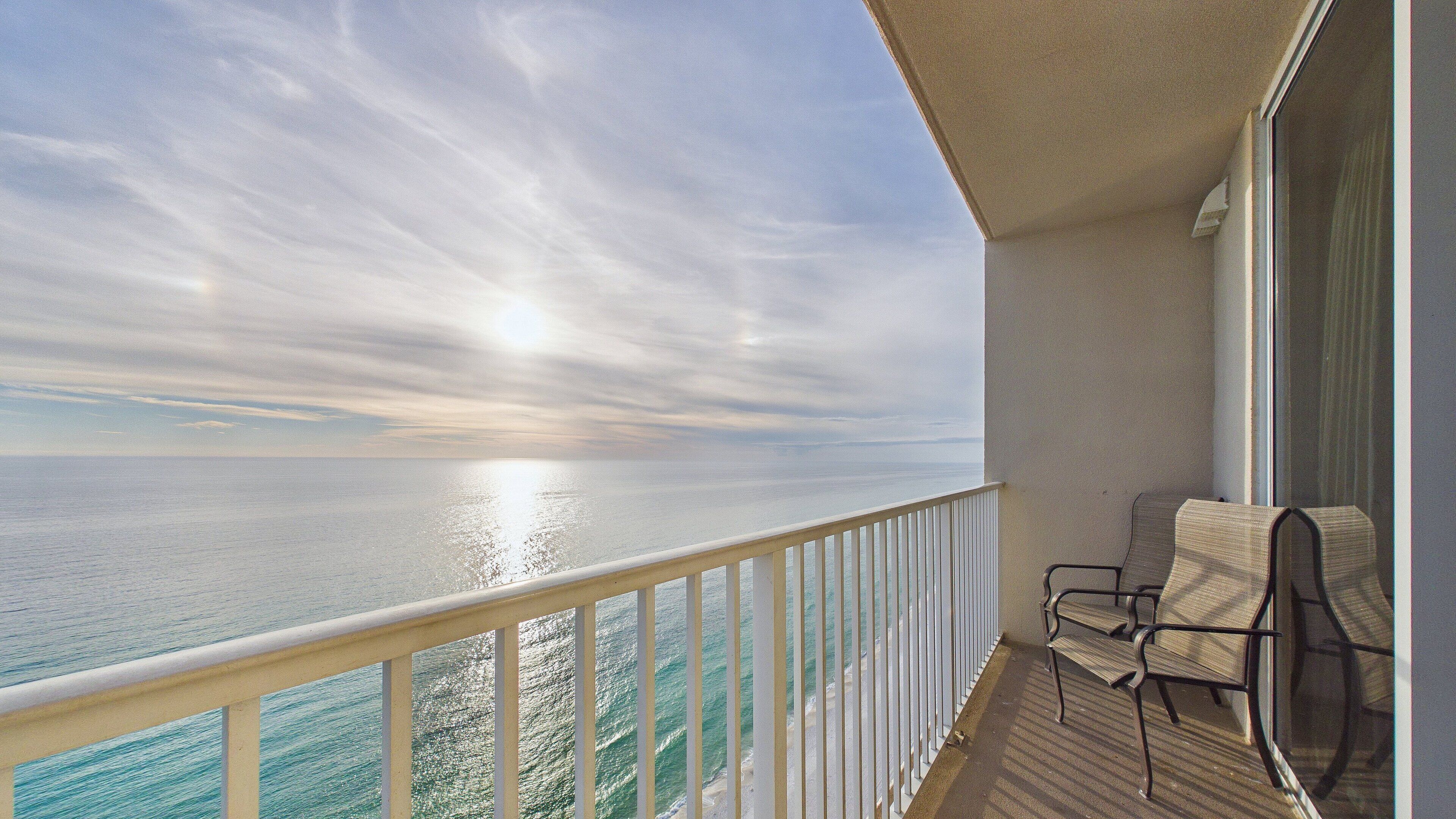 A balcony with a view of the ocean and a chair.