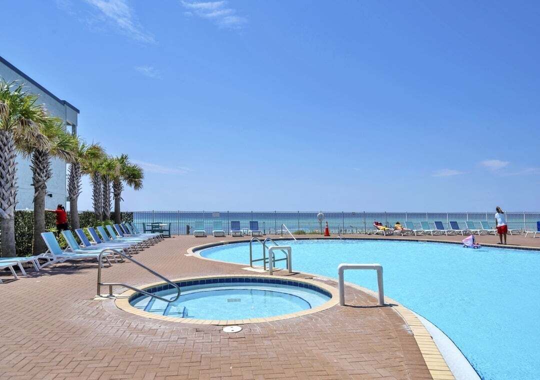 A pool area with lounge chairs and a view of the ocean.