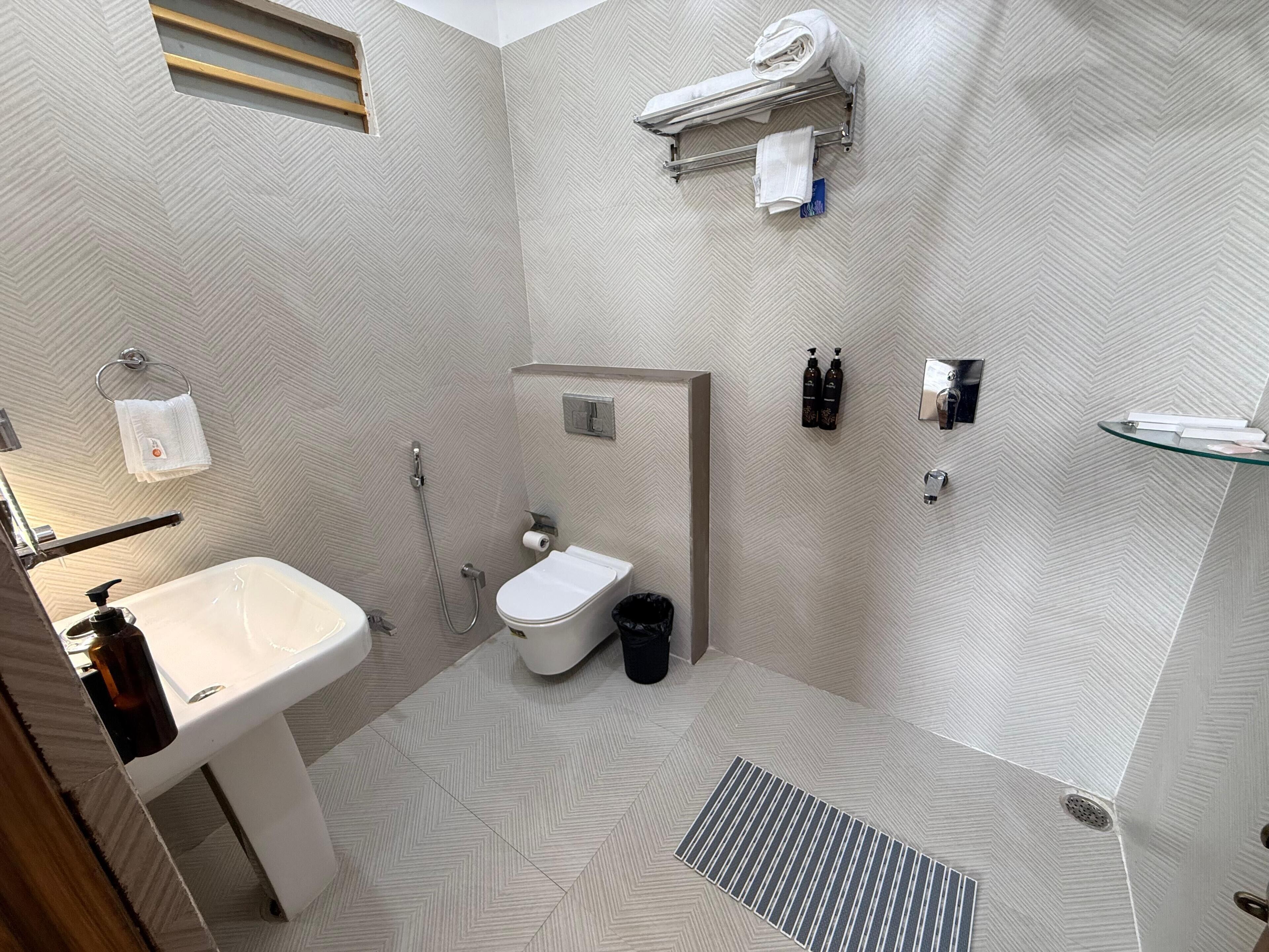 Een moderne badkamer met een wit wastafel, toilet en douche. Handdoeken en toiletartikelen hangen aan de muur.
