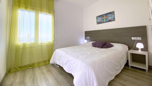 A bedroom with a bed, a nightstand, a lamp, a painting on the wall, and a window with sheer curtains. - Beautiful apartment 200m from the beach with terrace and garage in Roses (Roses)