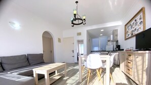 A modern living room with a sofa, a wooden coffee table, and a dining area with chairs and a table. A kitchen with a stove and cabinets is visible in the background. - Beautiful apartment 200m from the beach with terrace and garage in Roses (Roses)