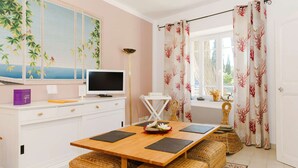 A modern kitchen with a wooden table, wicker stools, a white cabinet, a flat-screen TV, and decorative items. - Charming 2-Bedroom Cottage in Vineyard Estate, Near Narbonne-Plage, Sleeps 5, with WiFi and Parking (Narbonne-Narbonne Plage-Narbonne Plage)