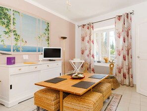 A modern kitchen with a wooden table, wicker stools, a white cabinet, a flat-screen TV, and decorative items. - Charming 2-Bedroom Cottage in Vineyard Estate, Near Narbonne-Plage, Sleeps 5, with WiFi and Parking (Narbonne-Narbonne Plage-Narbonne Plage)