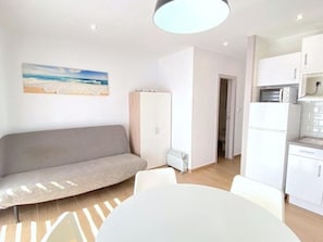 A modern living room with a sofa, a dining table, and a kitchen area with white cabinets and appliances. - Beautiful renovated beachfront apartment with private parking in Roses (Roses)