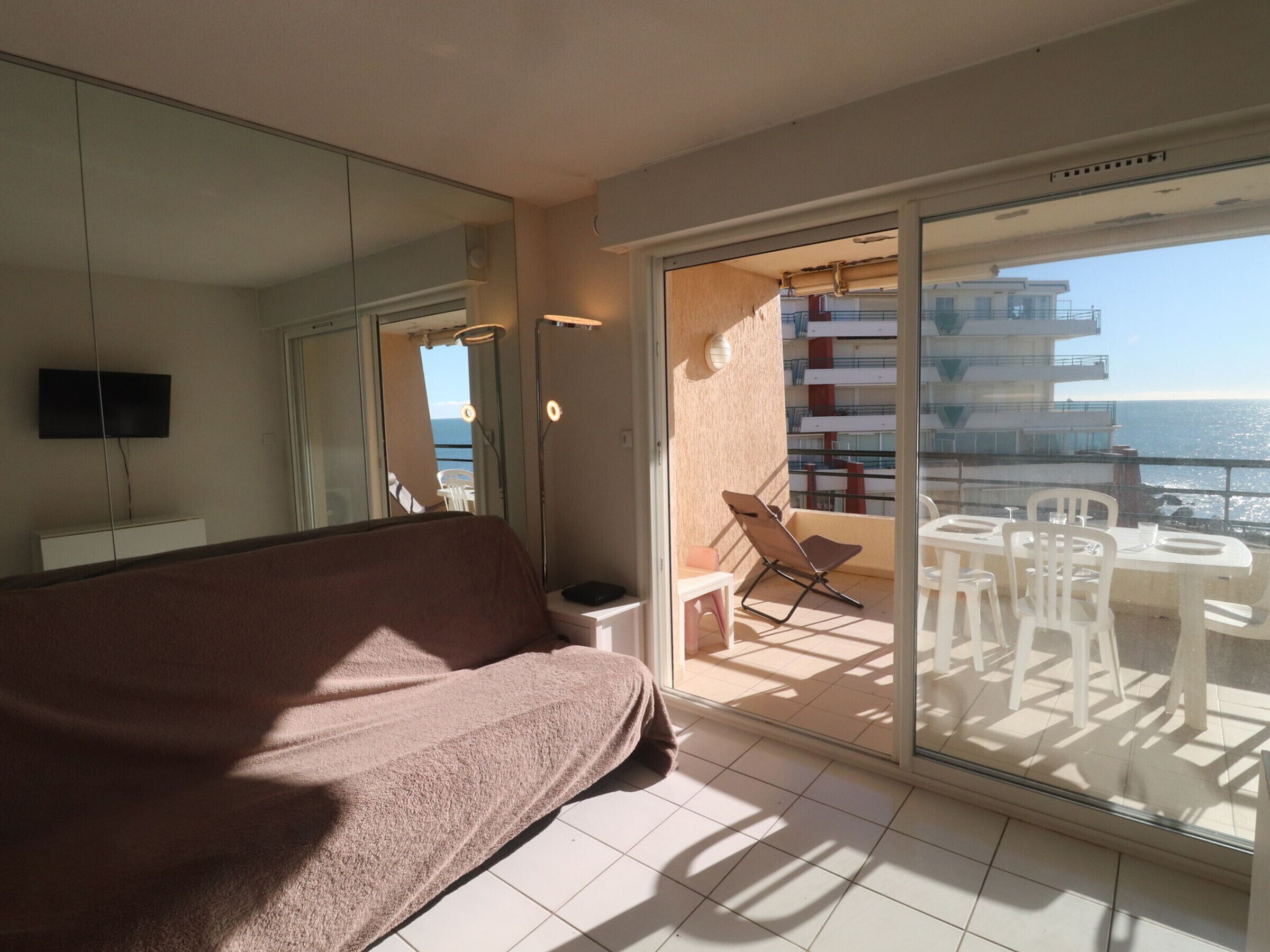 Ein Balkon mit Tisch, Stühlen, einer Couch und einem Fernseher.