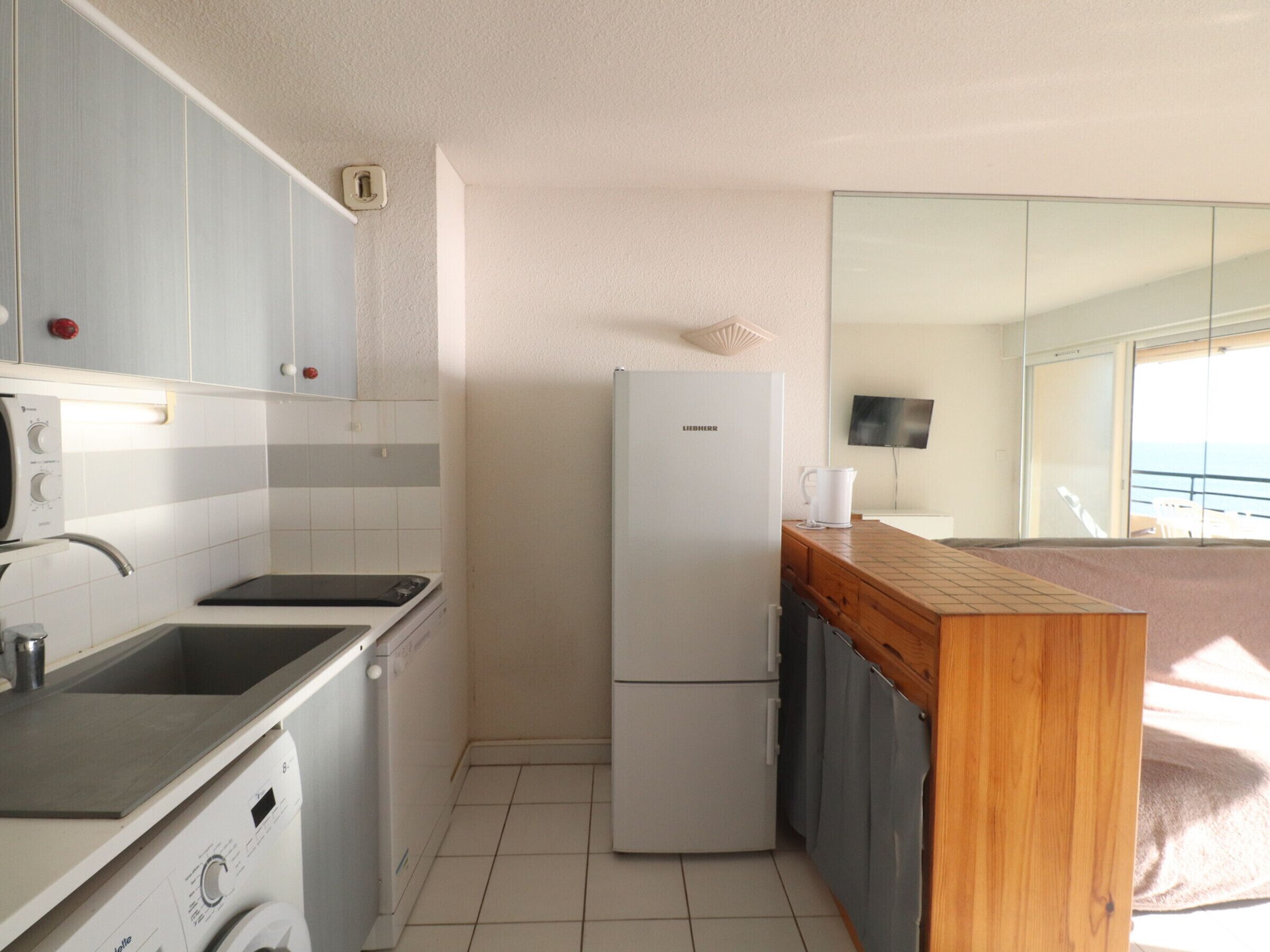 A compact kitchen with a built-in dishwasher, a refrigerator, and a wooden countertop.