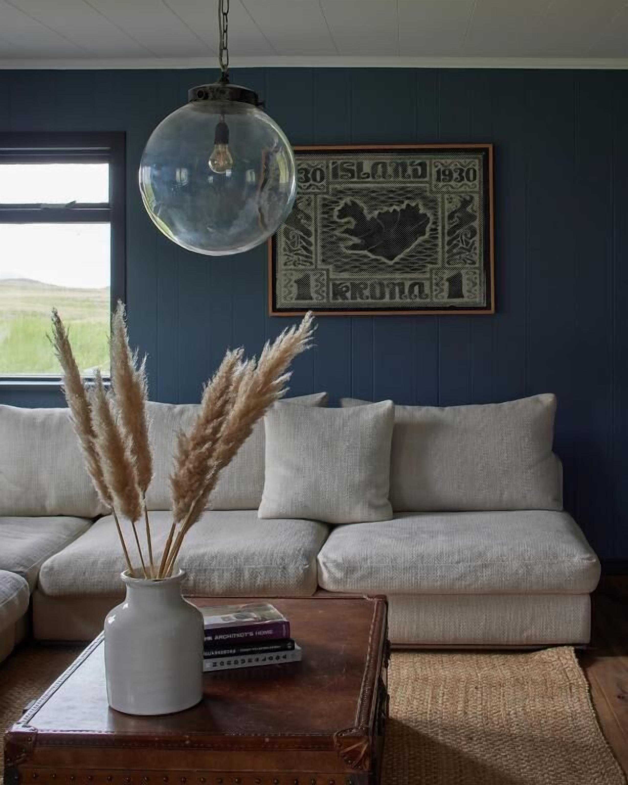 A living room with a white sofa, a glass pendant light, a framed artwork, and a vase with pampas grass.