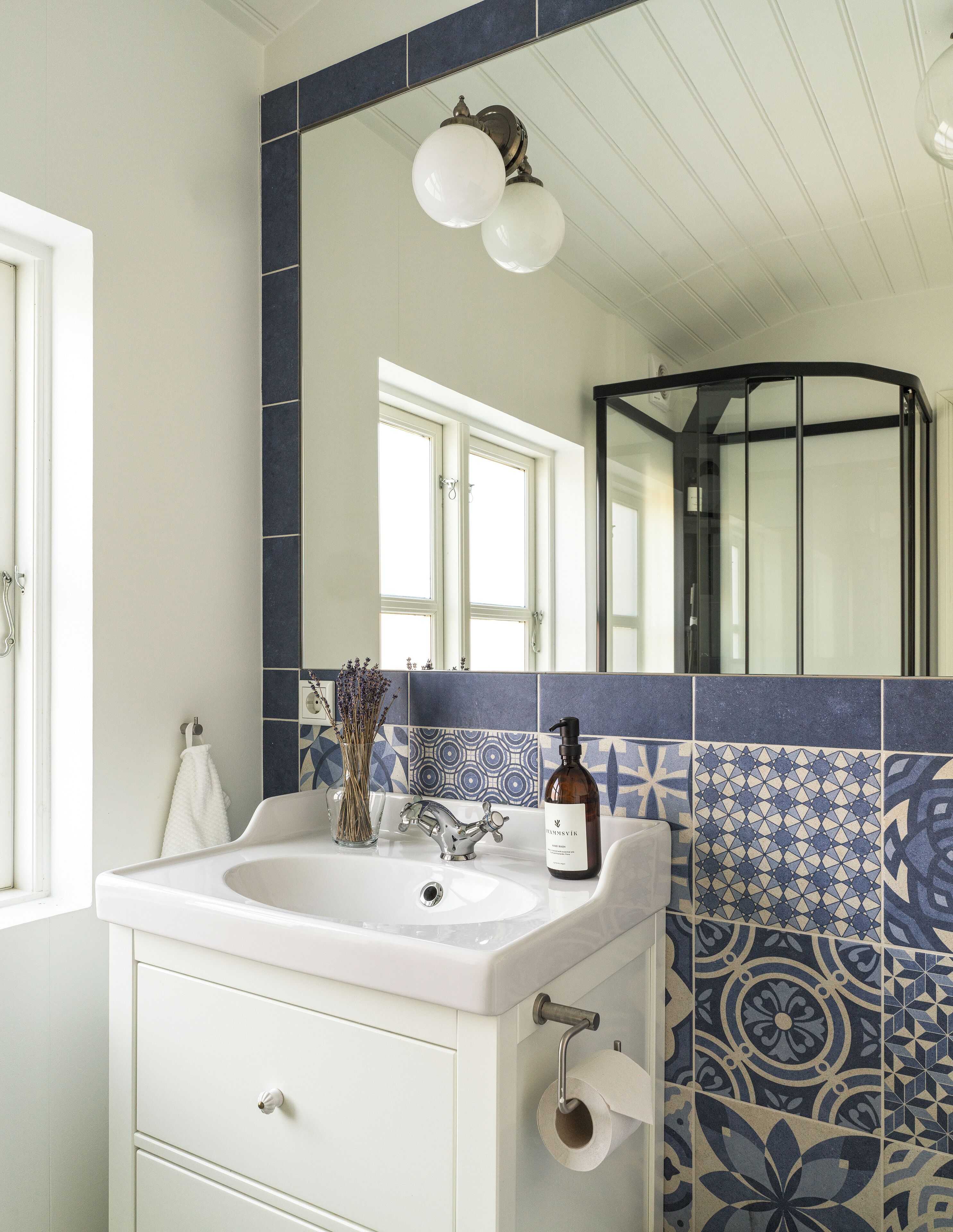 A bathroom with a white sink, a mirror, and a blue patterned tile wall.