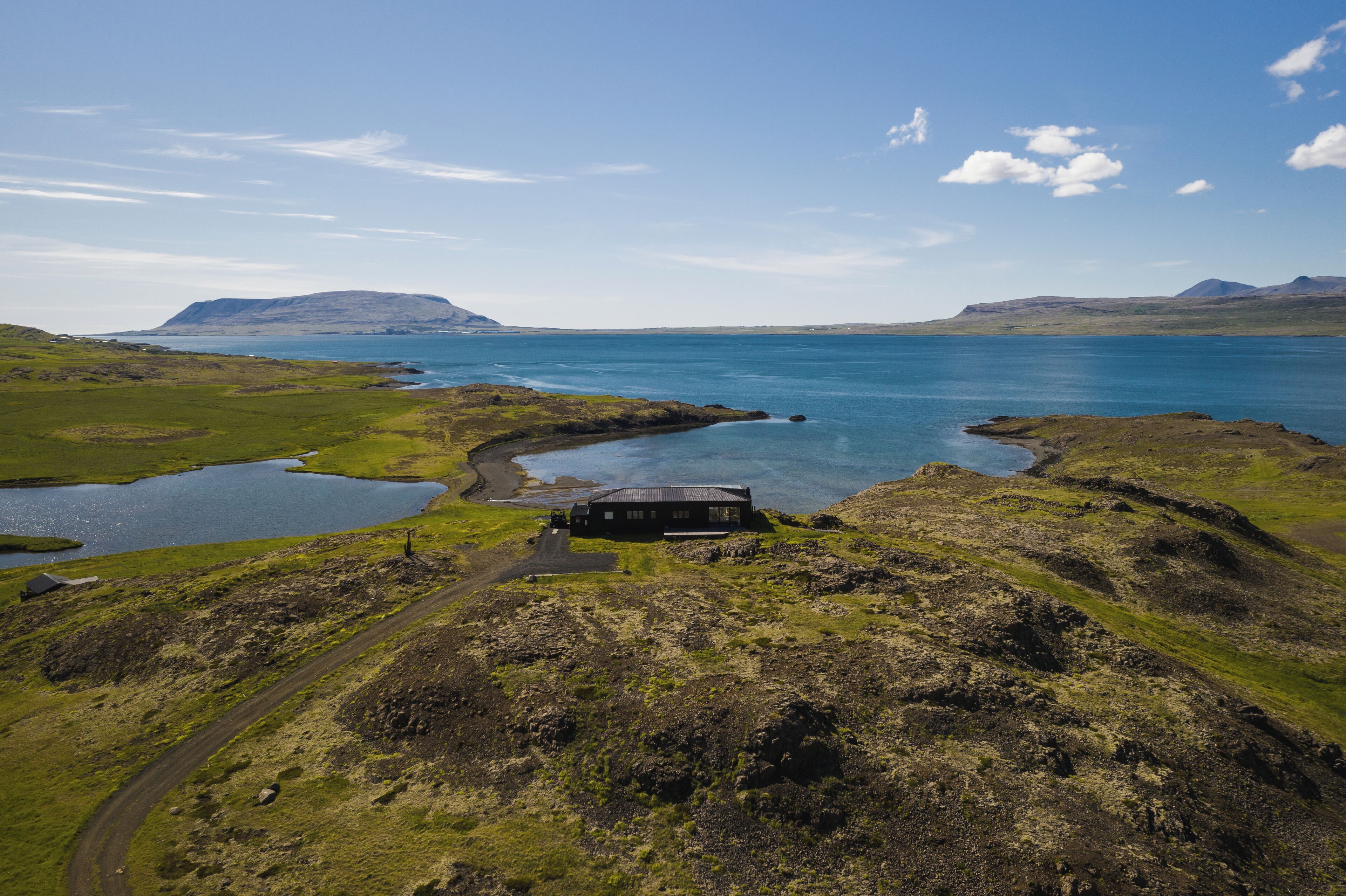 Un paisaje agreste y aislado, con una pequeña casa cerca de un lago, rodeado de colinas y cielos despejados.