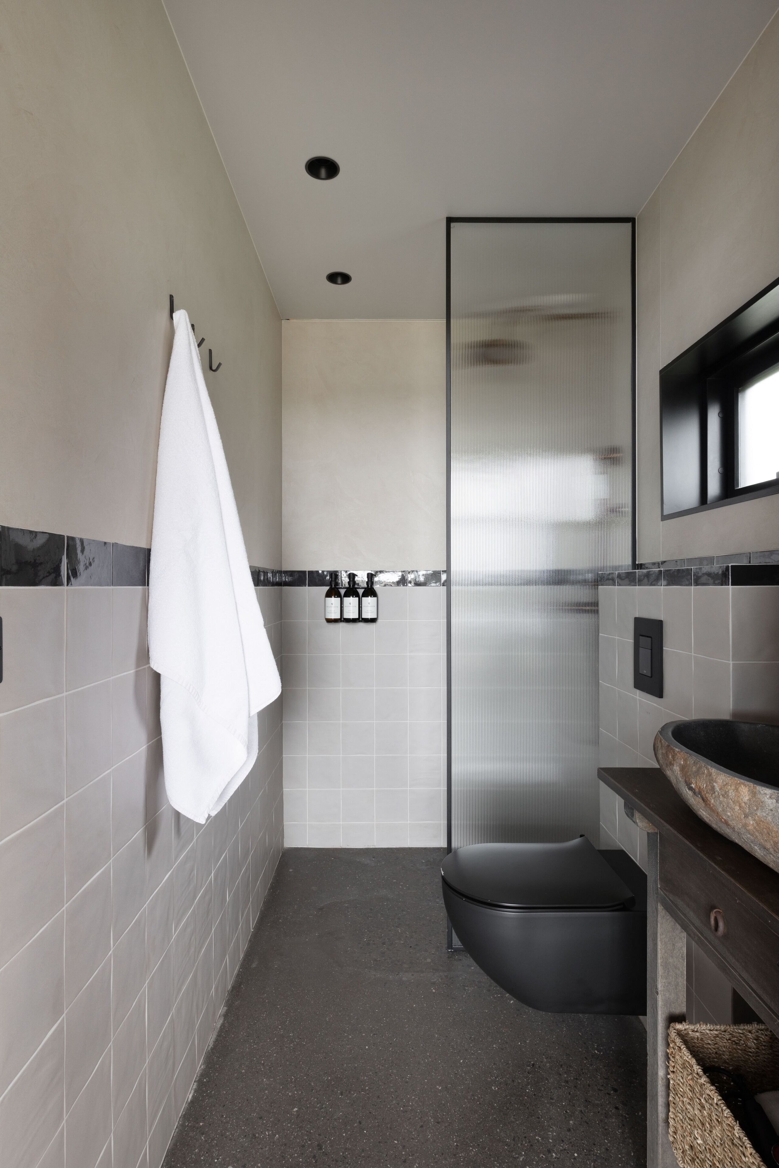 A modern bathroom with a glass shower enclosure, a black toilet, and a sink with a stone countertop.