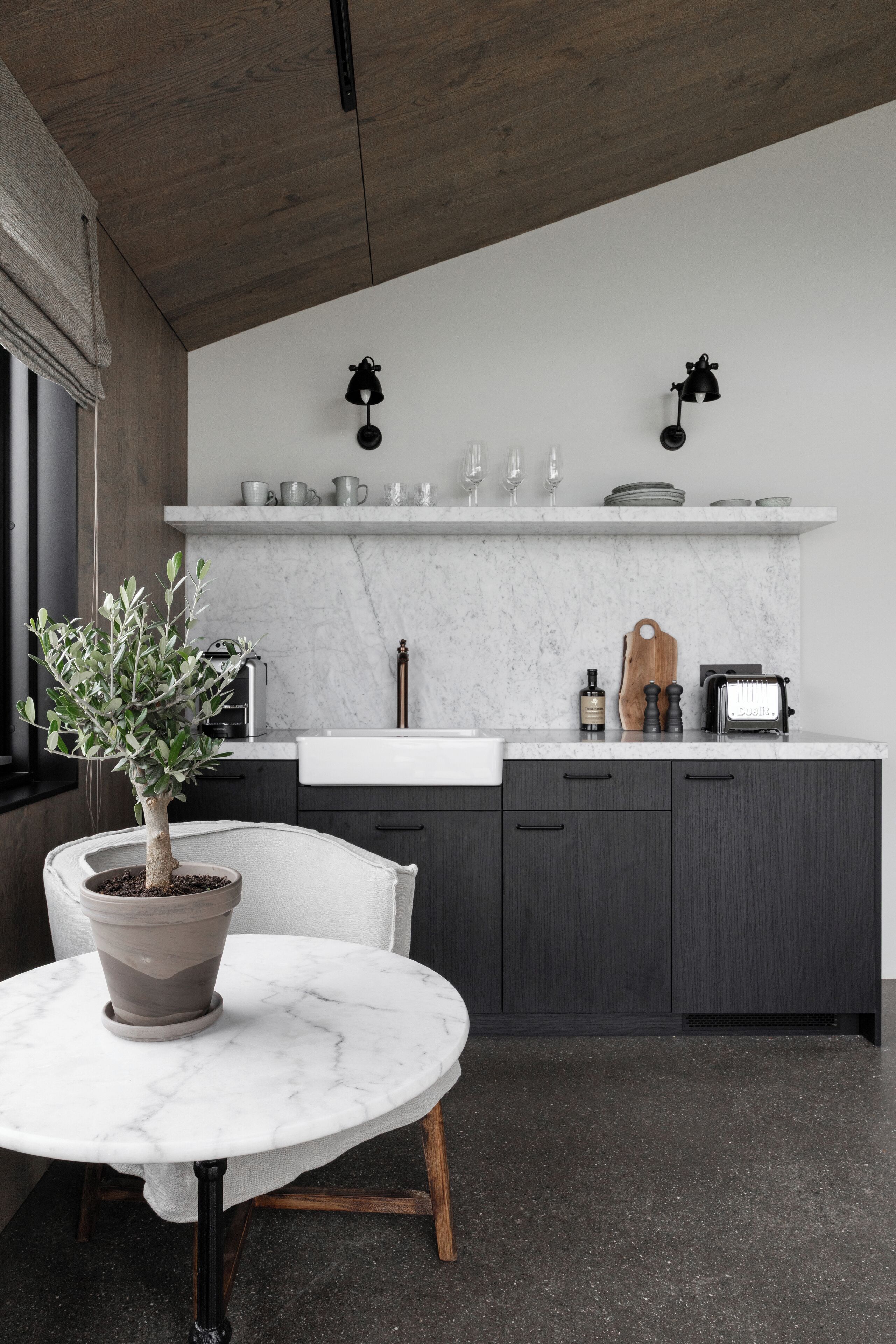 Una cocina moderna con armarios oscuros, encimera blanca y una planta en una mesa de mármol.