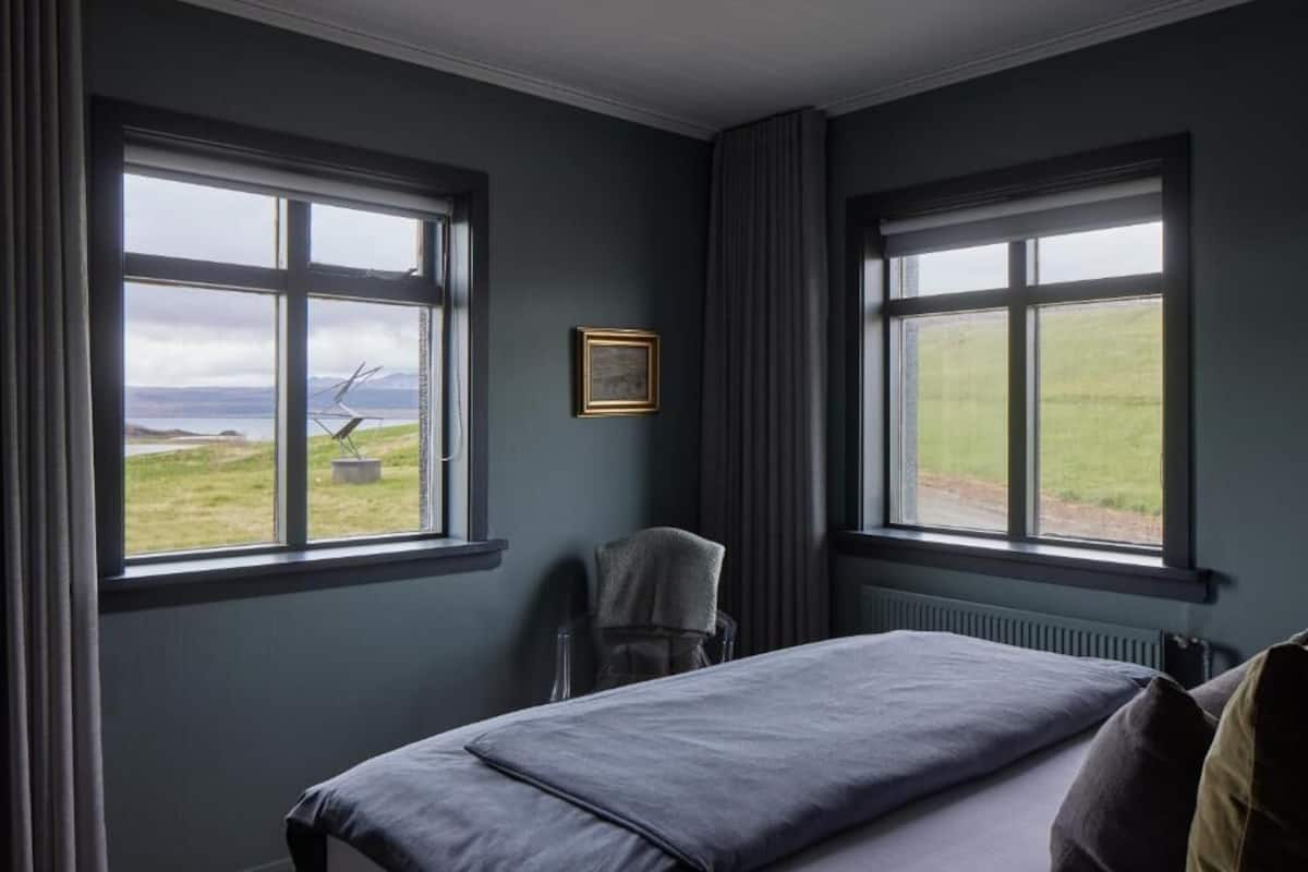 Una habitación con cama, una silla y dos ventanas que dan al exterior.