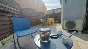 Een terras met een blauwe stoel, een ronde tafel met een waterkoker en een Mitsubishi airconditioner.
