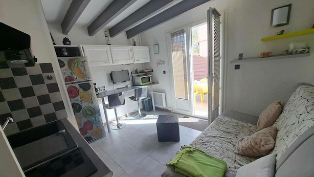 Een compacte woonruimte met een kitchenette, een bank met kussens en een eethoek met een tafel en stoelen.