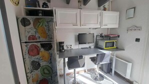 Een kleine keuken met een koelkast, magnetron, en een eethoekje met een stoel.
