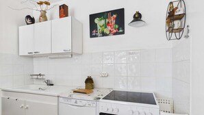 Ett kök med vita skåp, diskmaskin, ugn och en vägghylla med dekorativa föremål.