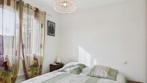 Ett sovrum med en säng, ett sängbord, en lampa och ett fönster med gardiner.