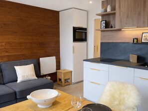 Eine moderne Küche mit weißen Schränken, einer Holz Arbeitsplatte und einer Mikrowelle. Auf der Arbeitsplatte steht ein kleiner Holzhocker und eine weiße Schüssel.