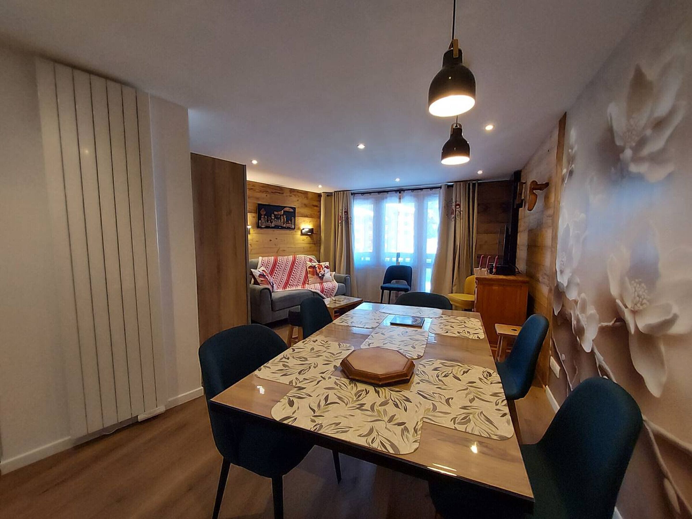 A dining area with a table set for four, surrounded by chairs. There is a sofa and a television in the background.