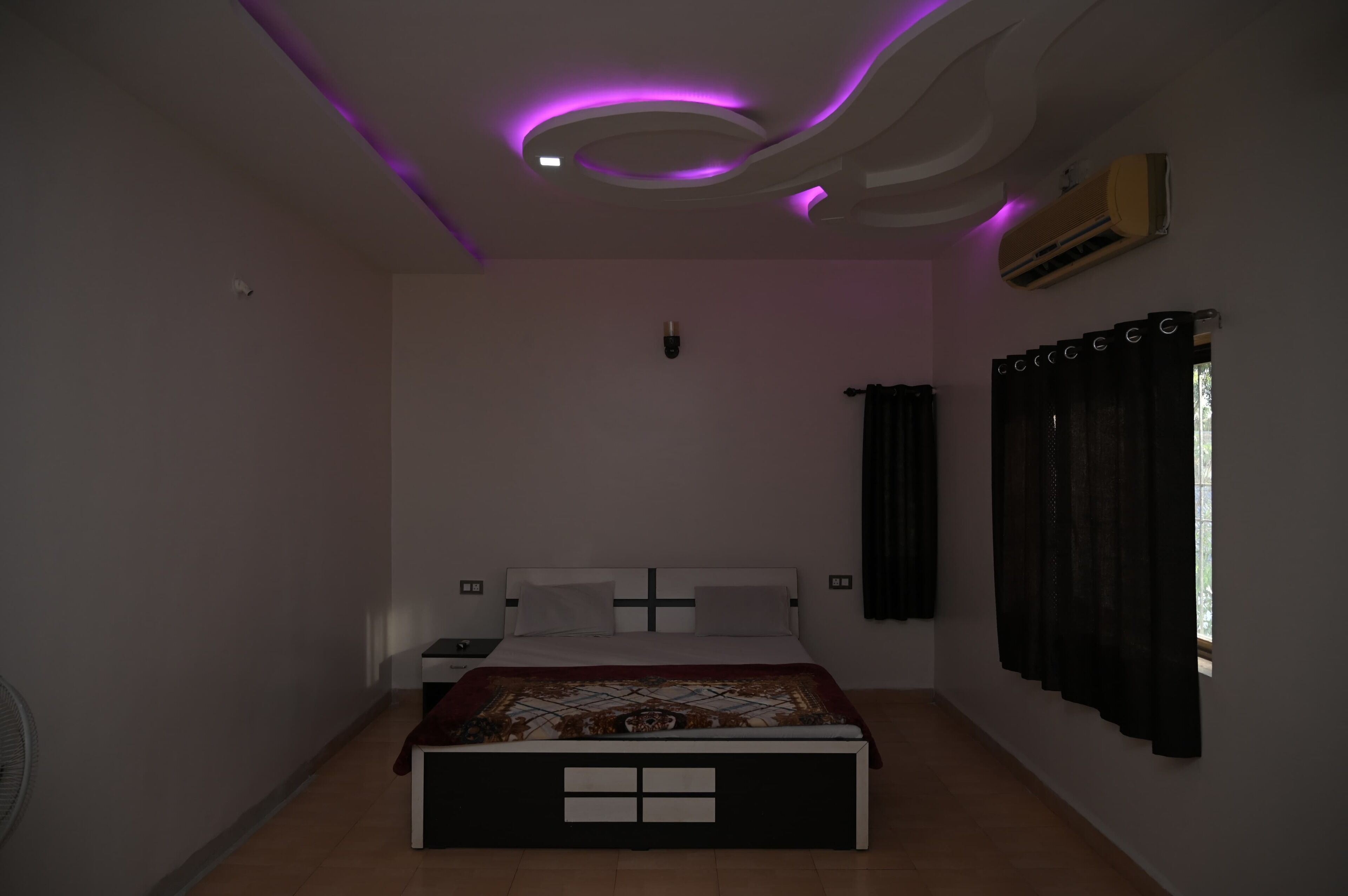 A bedroom with a bed, a ceiling light, and a window with curtains.